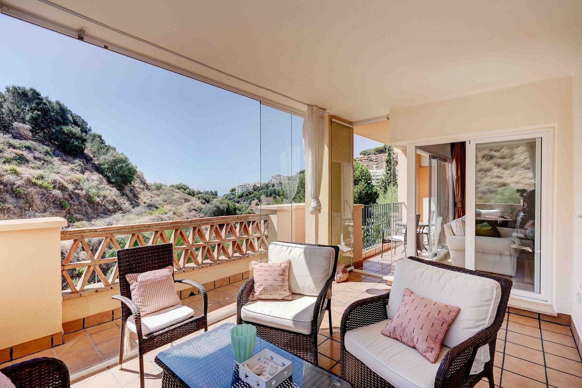 A covered terrace with comfortable seating and a beautiful view of a lush, green hillside on a sunny day.