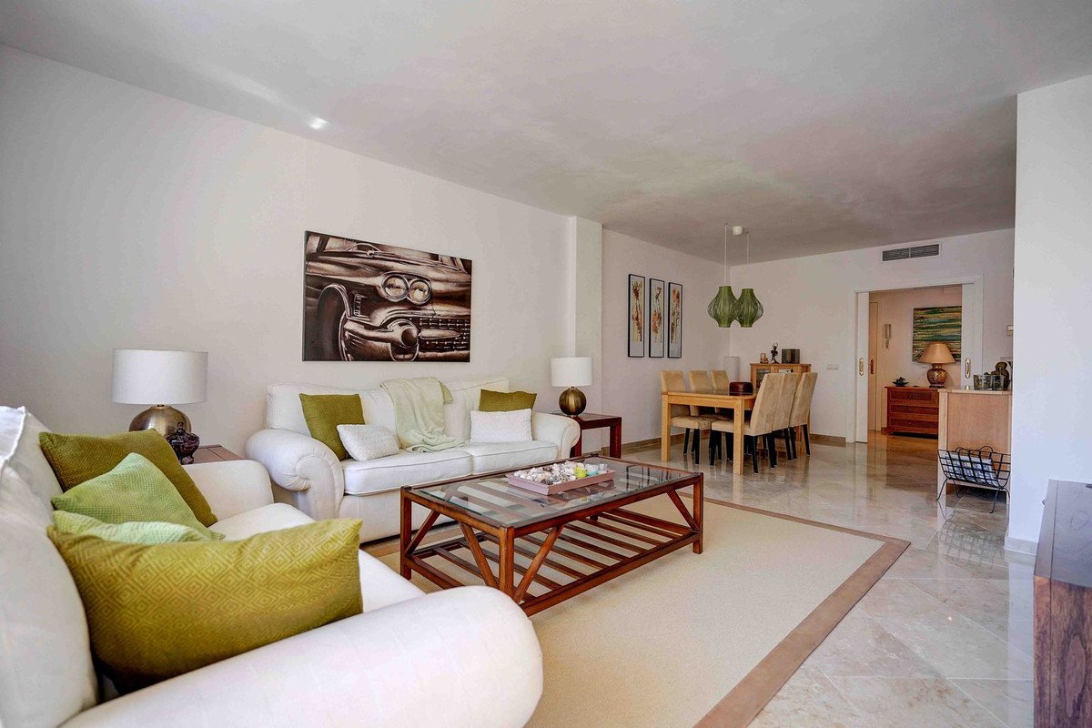 A bright living and dining room with white sofas, a wooden coffee table, and a dining set, featuring modern art and decorative lamps.