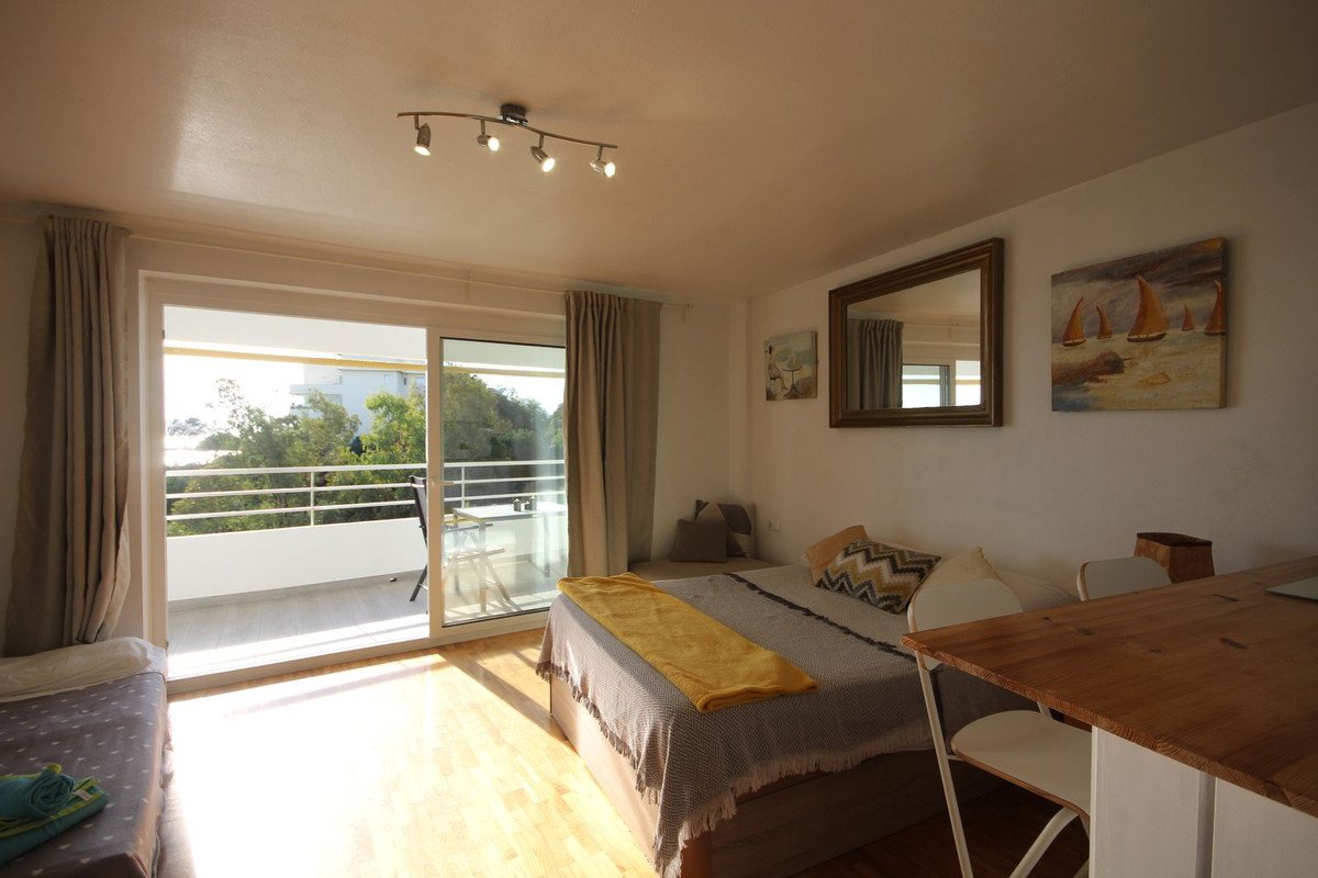 Bedroom with a double bed, a single bed, and a balcony with a sea view overlooking trees.