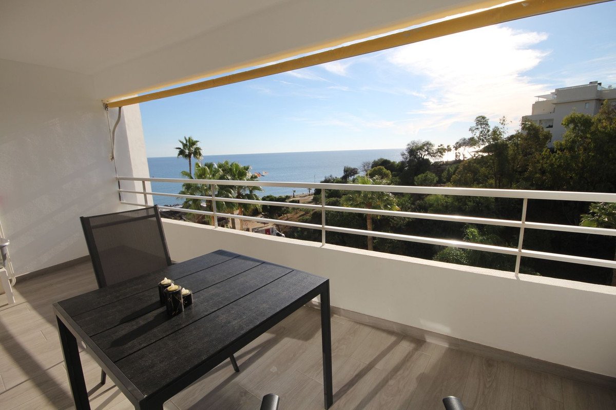 Balcony with table and chairs offering a sea view with palm trees and lush greenery.