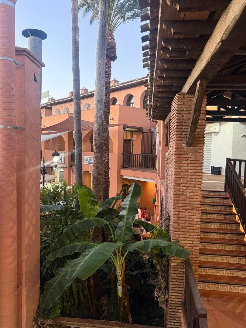 View from a balcony of a courtyard with lush tropical plants, palm trees, and buildings with Spanish architecture.