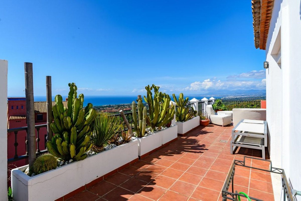 A spacious terrace with cacti, white outdoor furniture, and a panoramic view of the sea and distant landscape under a clear blue sky.