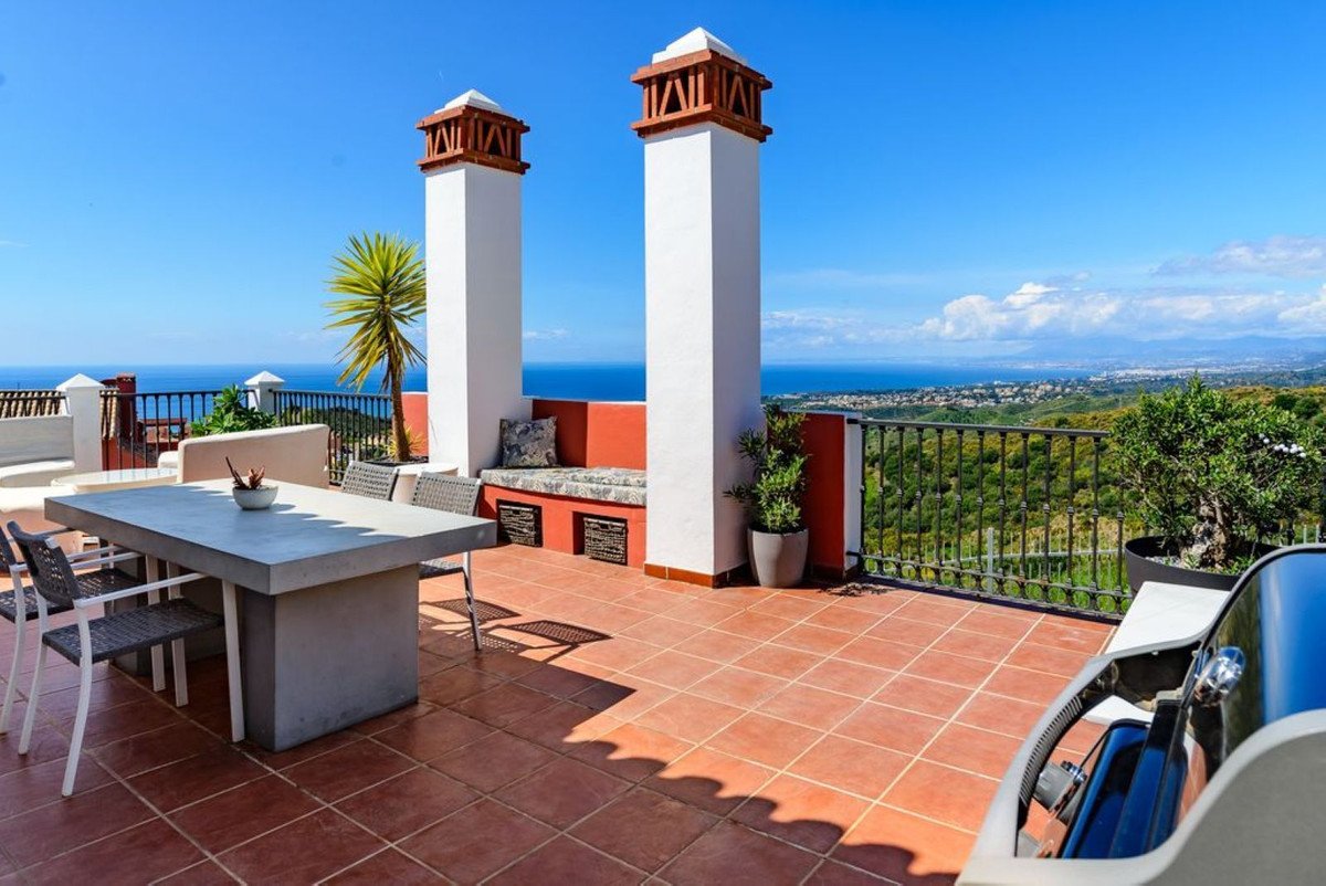 Terrace with dining table, seating area, two chimneys, and a panoramic view of the sea and coastline.