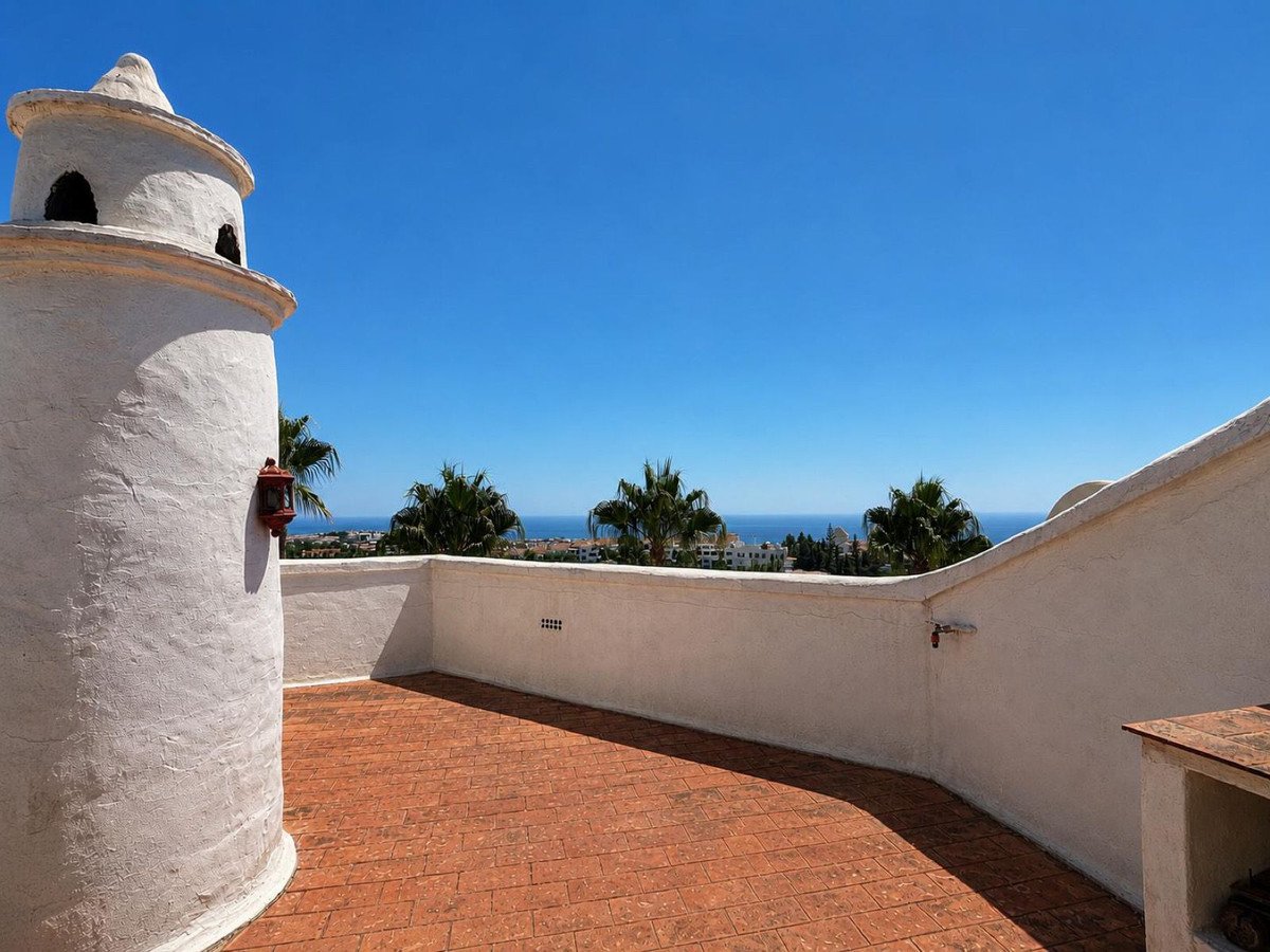 Terrace with a unique architectural element and a beautiful sea view, surrounded by palm trees under a clear blue sky.