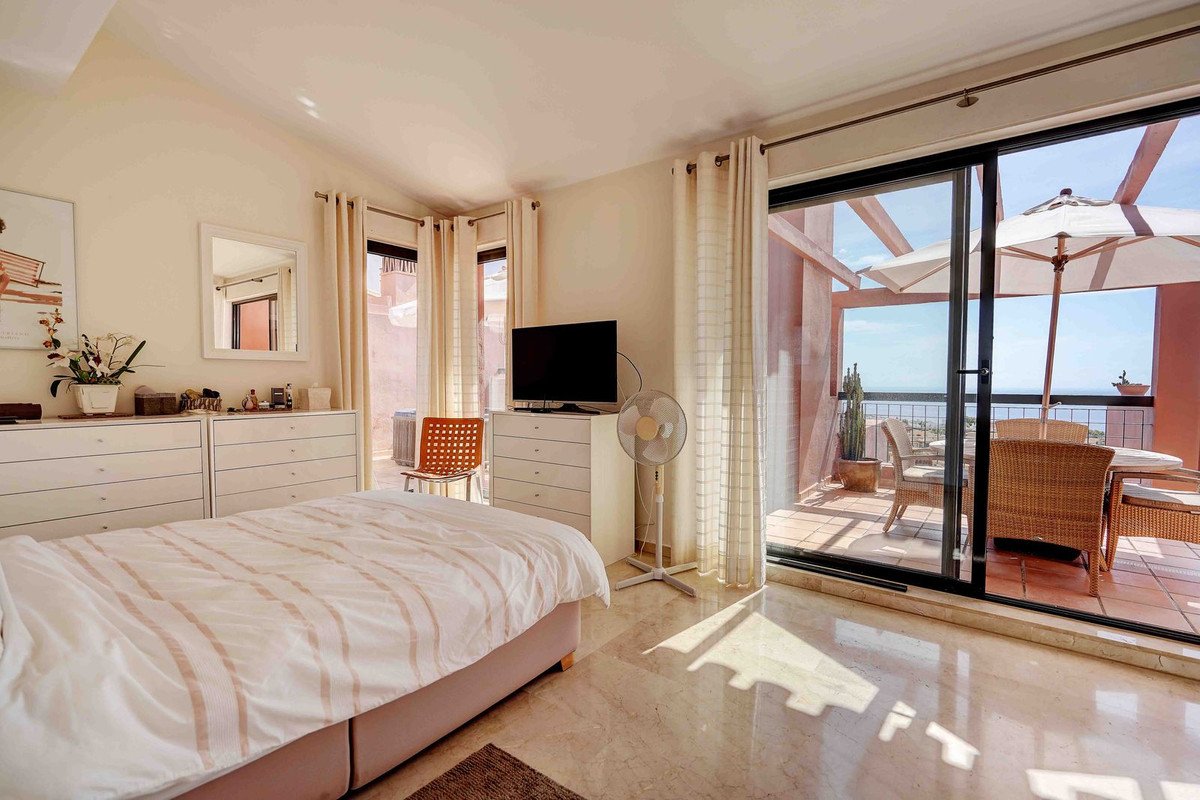 Bright bedroom with a large bed, leading to a spacious terrace with sea views and outdoor seating.