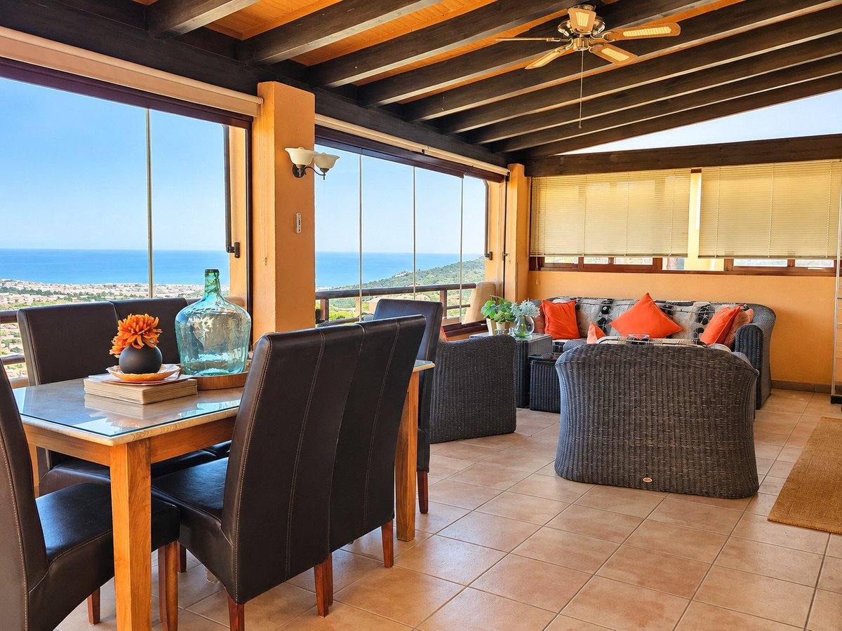 Enclosed terrace with dining table, seating area, and stunning panoramic sea views.