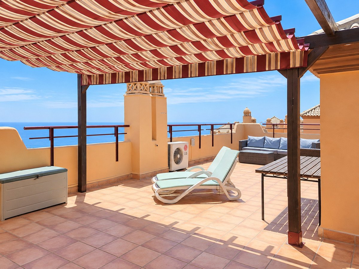 Spacious terrace with sea view, featuring lounge seating, a sun lounger, and a dining table under a striped awning.