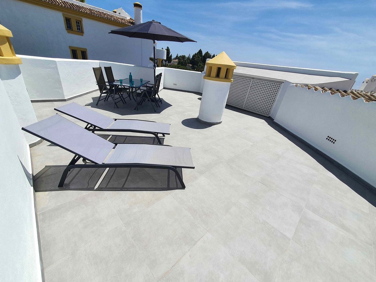 Rooftop terrace with sun loungers, dining set, and white walls under blue sky