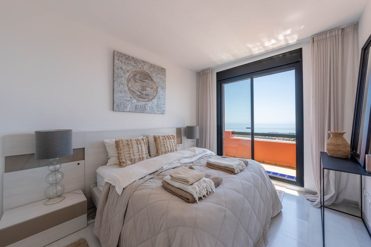 Comfortable bedroom with a large bed, overlooking the sea from a balcony accessible through sliding glass doors.