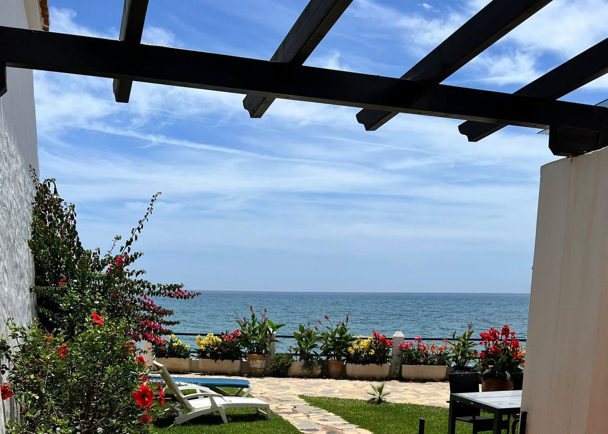 Terrace with sea view, lounge chairs, and flowering plants under a pergola on a sunny day.