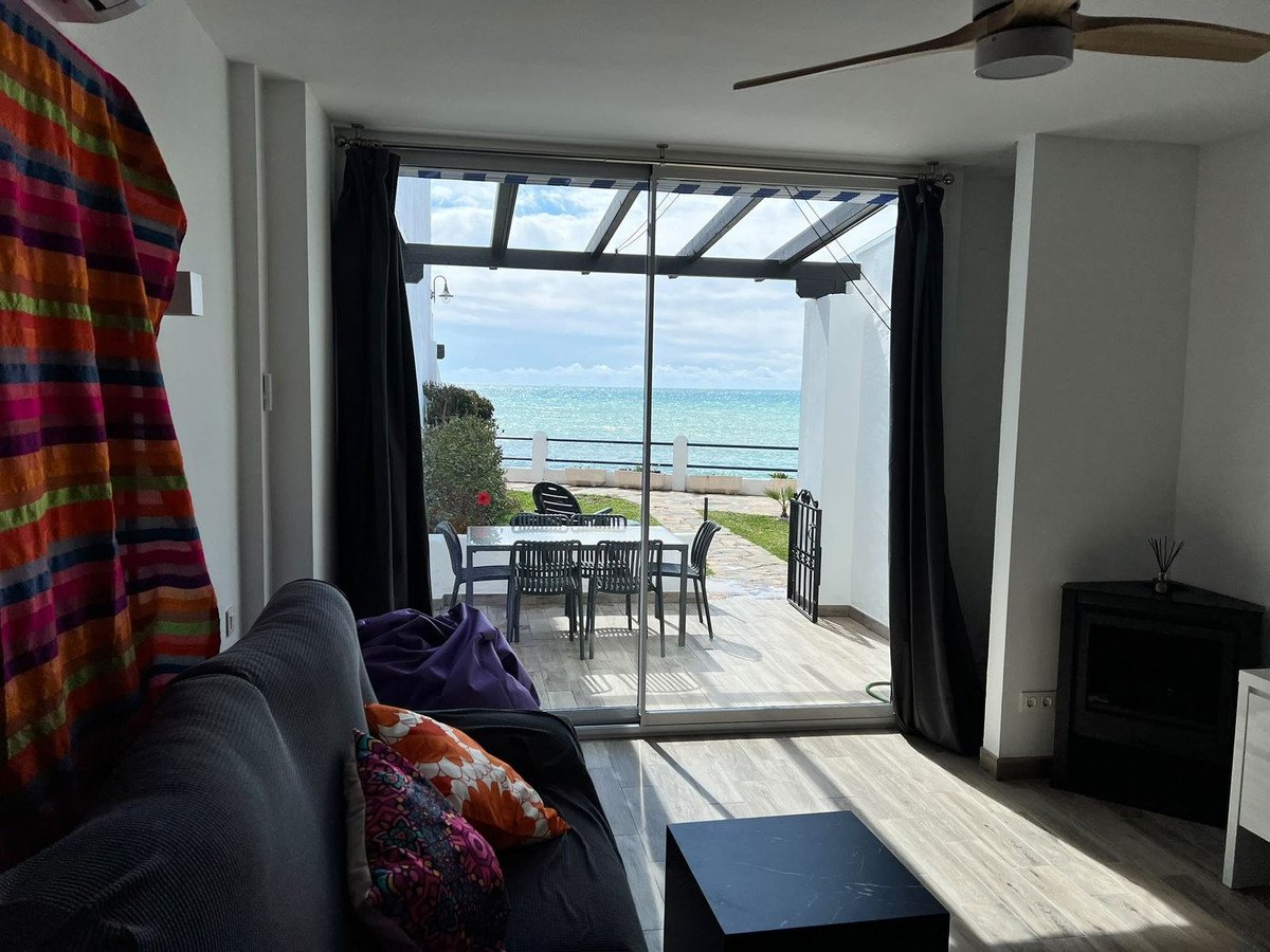 Living room with sofa and colorful pillows opens to a patio with dining set and a beautiful sea view.
