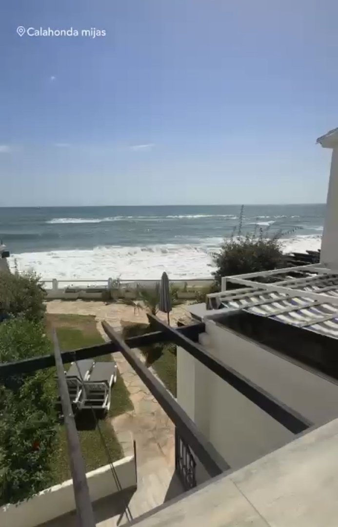 Terrace overlooking the sea with waves crashing on the shore and lounge chairs visible below.