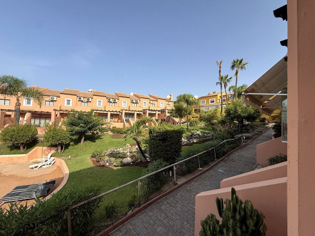 View of a manicured garden with lounge chairs and apartments in the background under a clear blue sky.