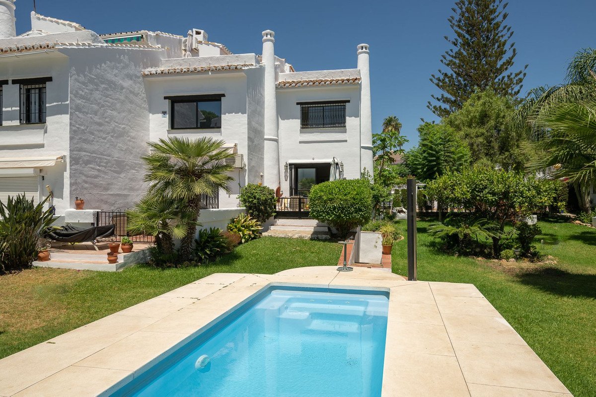 A white villa with a private pool, lush garden, and palm trees under a clear blue sky.