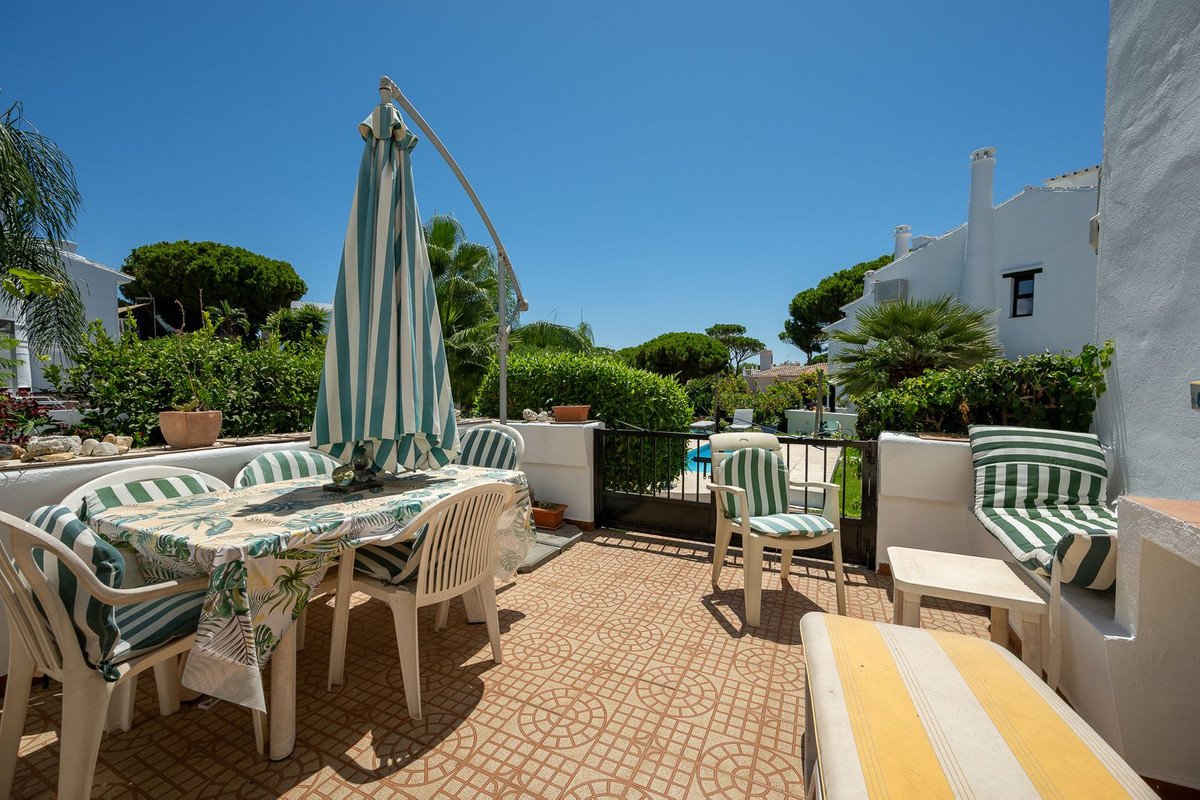 Sunlit patio with striped furniture, umbrella, and pool view in a white villa.
