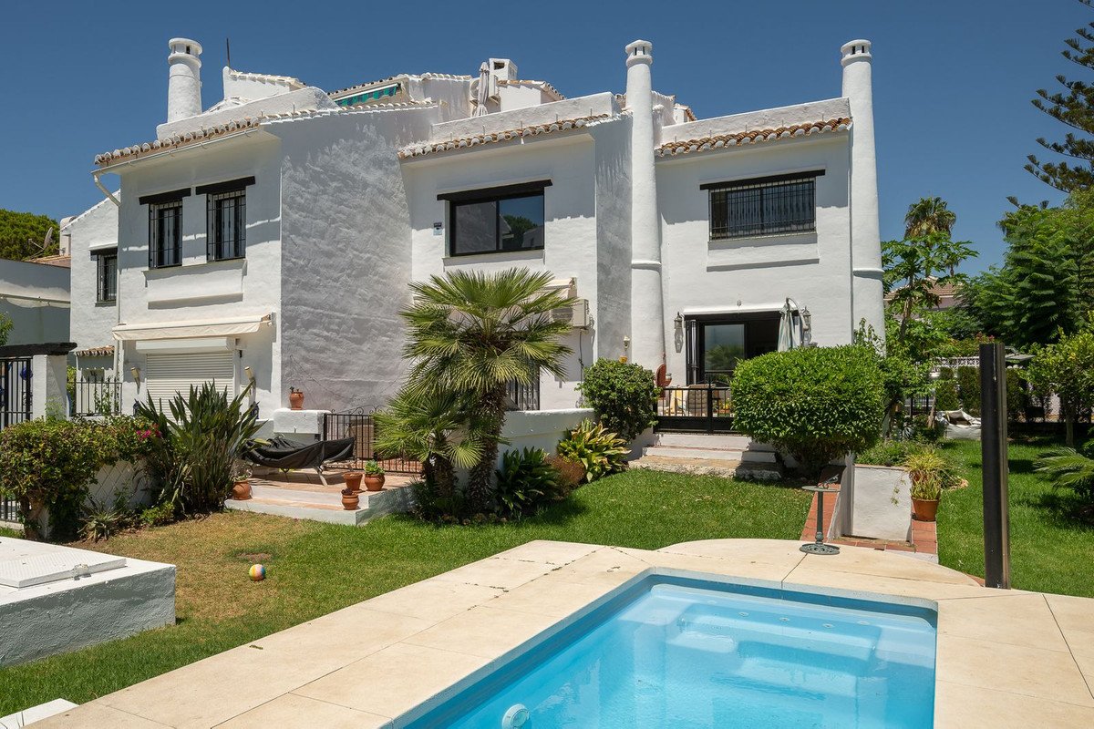White villa with pool, palm trees, and garden under clear blue sky.