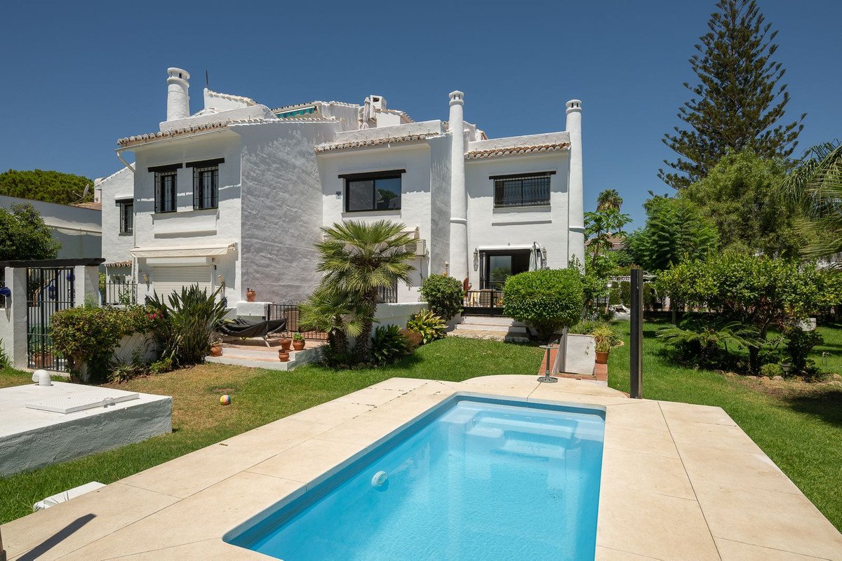 White villa with pool, palm trees, and garden under clear blue sky.