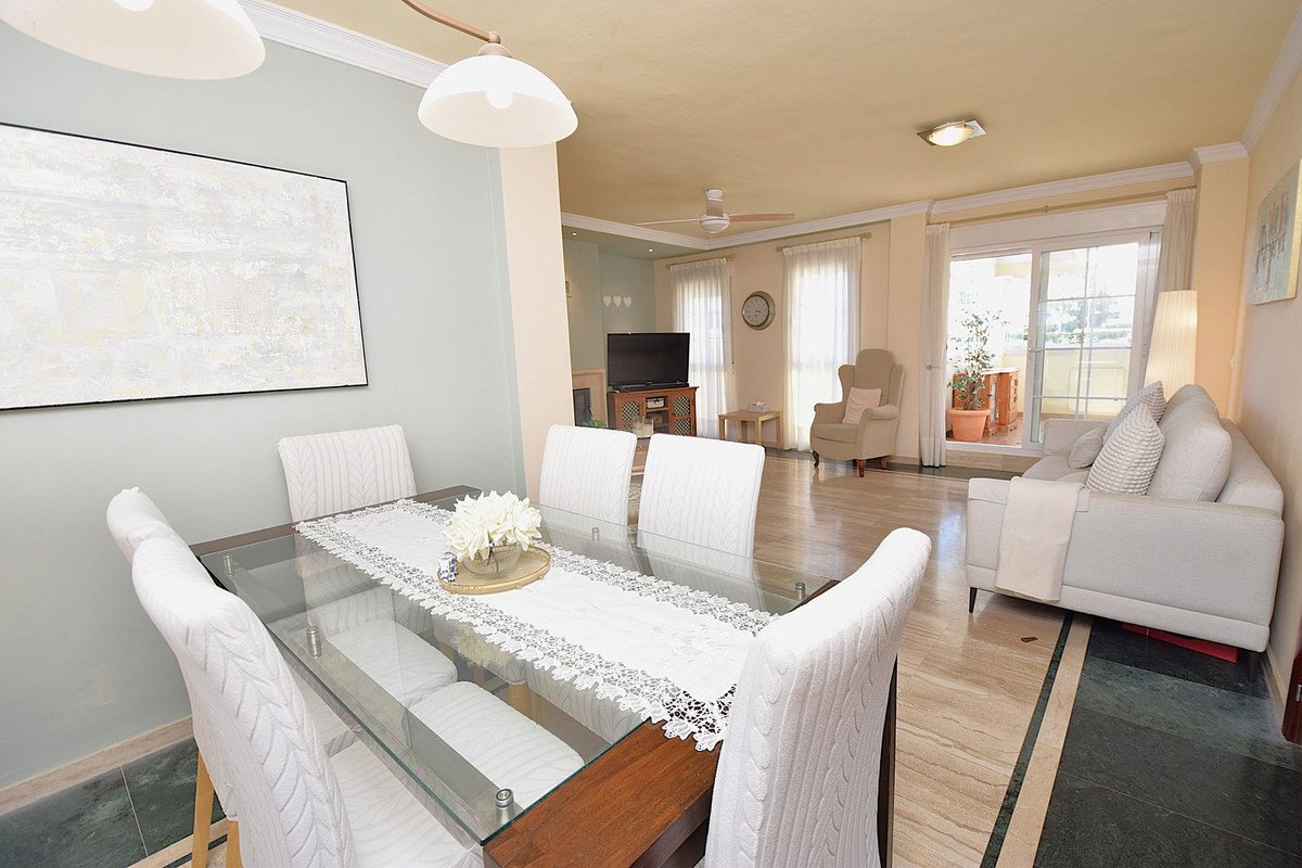 Open-plan dining and living room with glass table, white chairs, sofa, and sliding doors