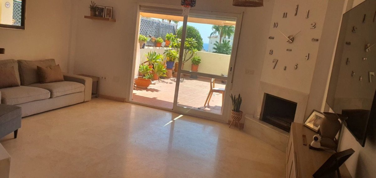 Living room with a comfortable sofa, large sliding glass doors opening to a terrace with plants and a distant sea view.
