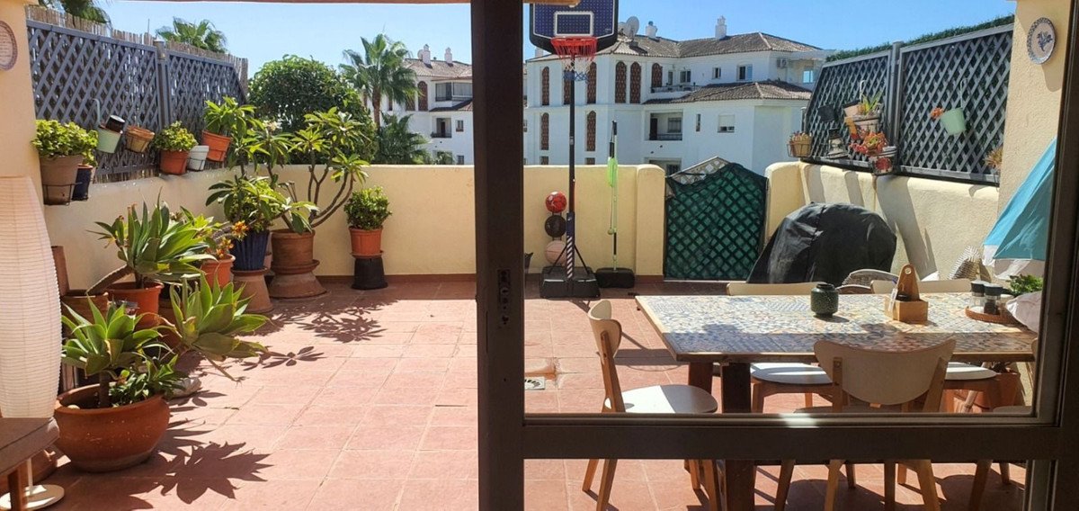 Terrace with potted plants, a dining table with chairs, and buildings in the background.