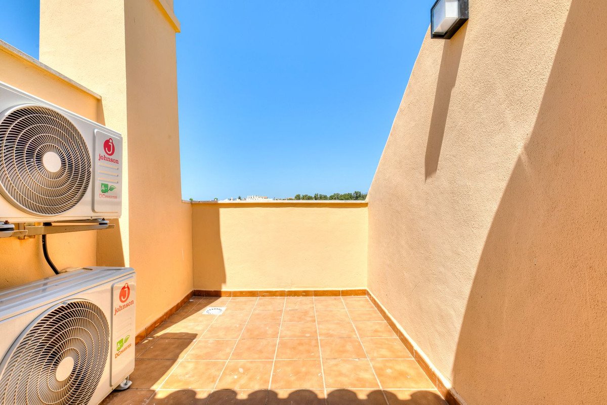 An outdoor terrace with two air conditioning units and a view of the sky and distant buildings.