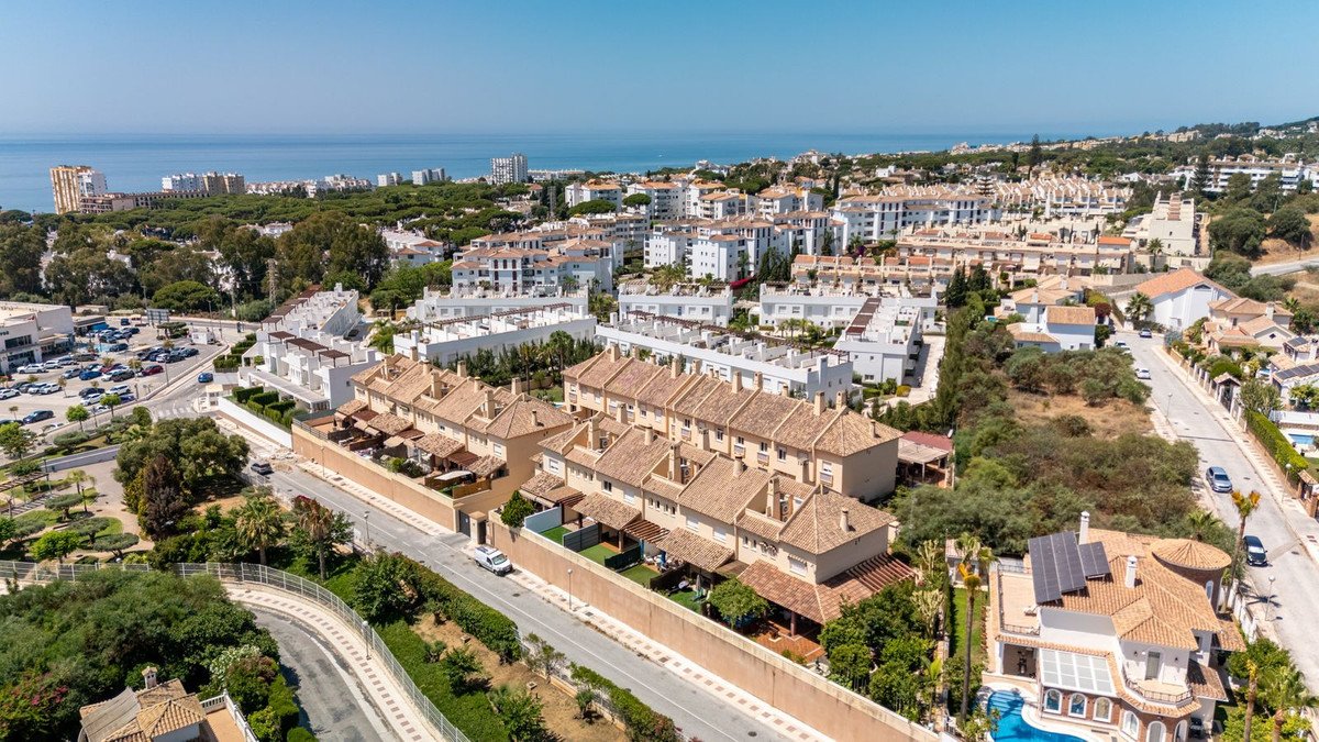 Aerial view of a townhouse complex with a distant sea view and surrounding residential buildings and greenery.