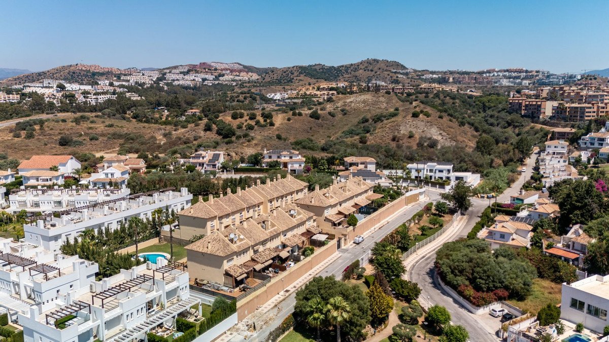 Aerial view of modern townhouses with pools, overlooking a hilly landscape with residential buildings.