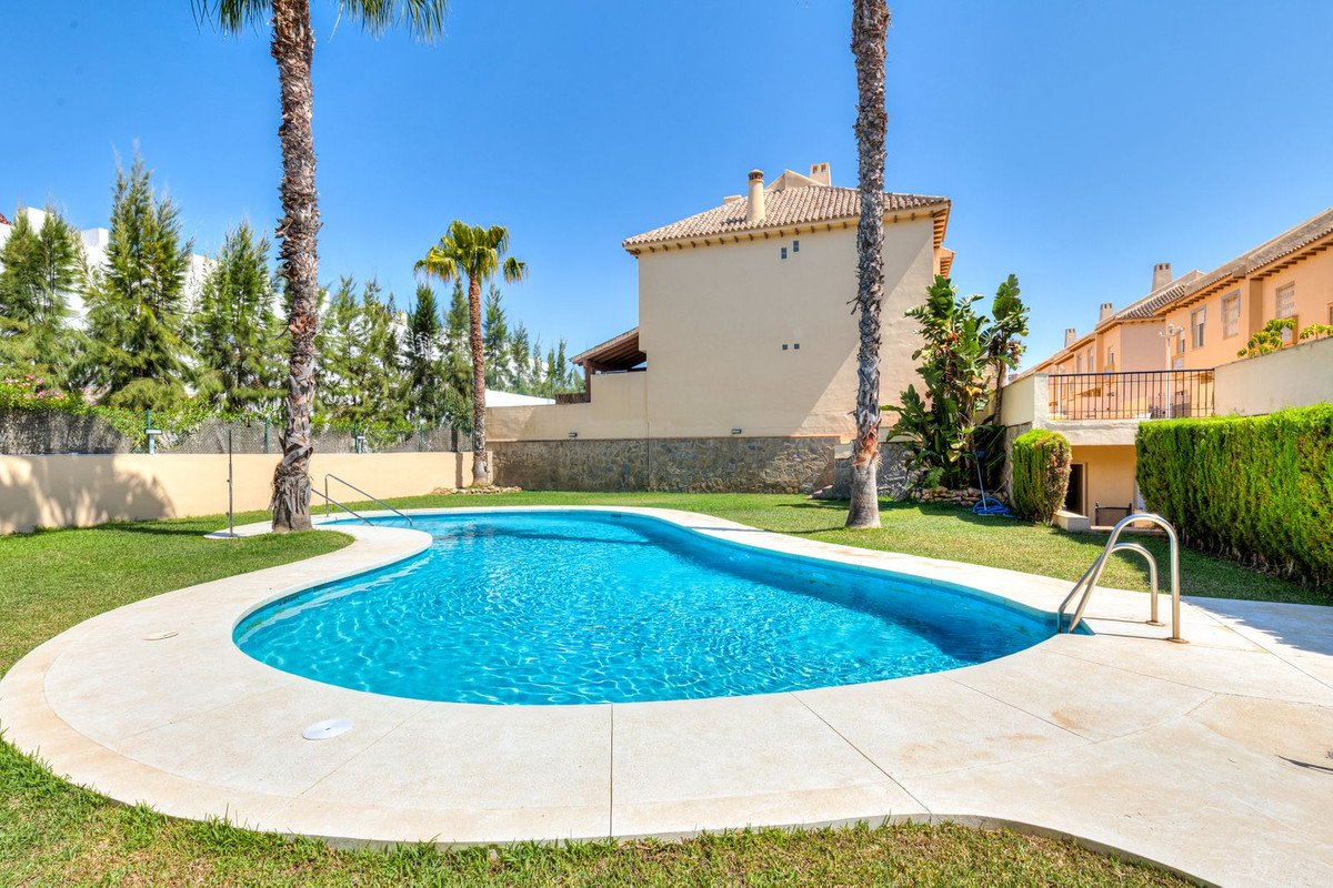 A private swimming pool with a curving design, surrounded by green grass and palm trees, with houses in the background.