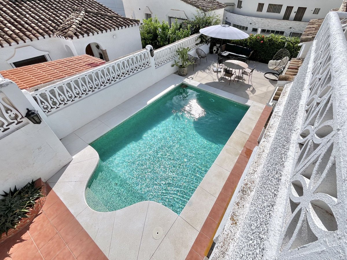 A sparkling turquoise swimming pool with an outdoor seating area and umbrella on a sunny day, typical of a Spanish villa.