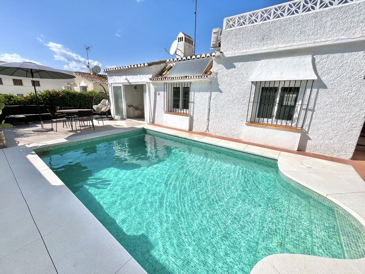 A private swimming pool and outdoor seating area with a patio and a white house.