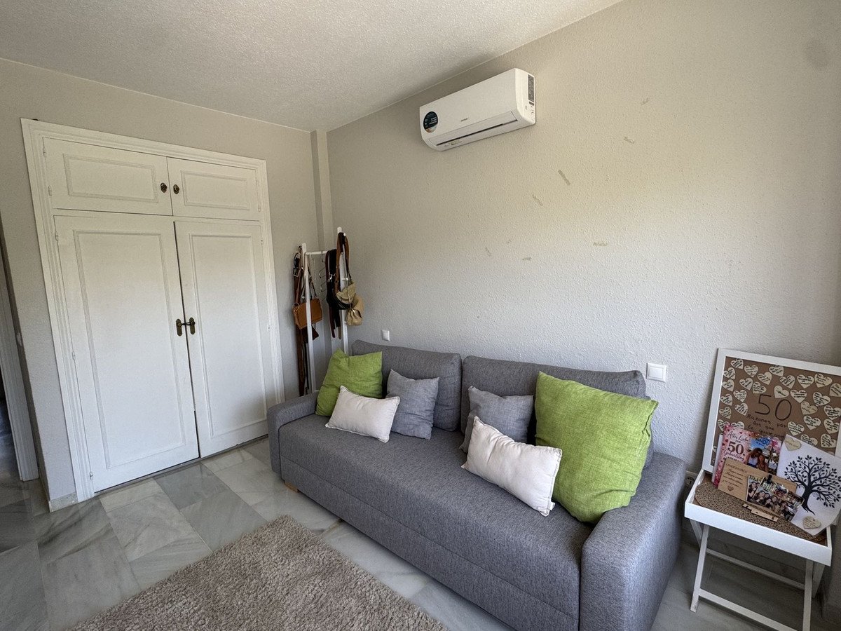 A grey sofa with green and white cushions in a room with a large white wardrobe and an air conditioning unit.