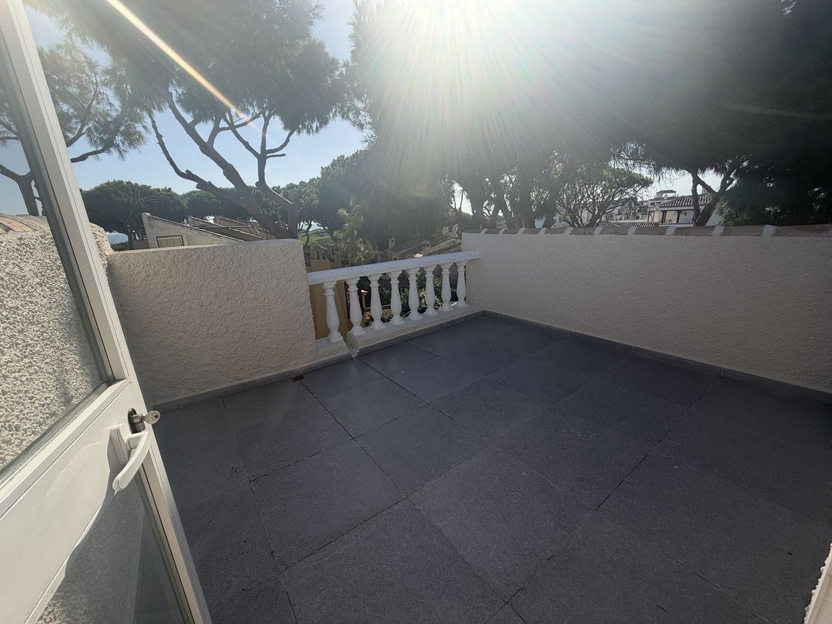 Spacious balcony with tiled floor and ornate railing, offering a view of trees and distant rooftops.