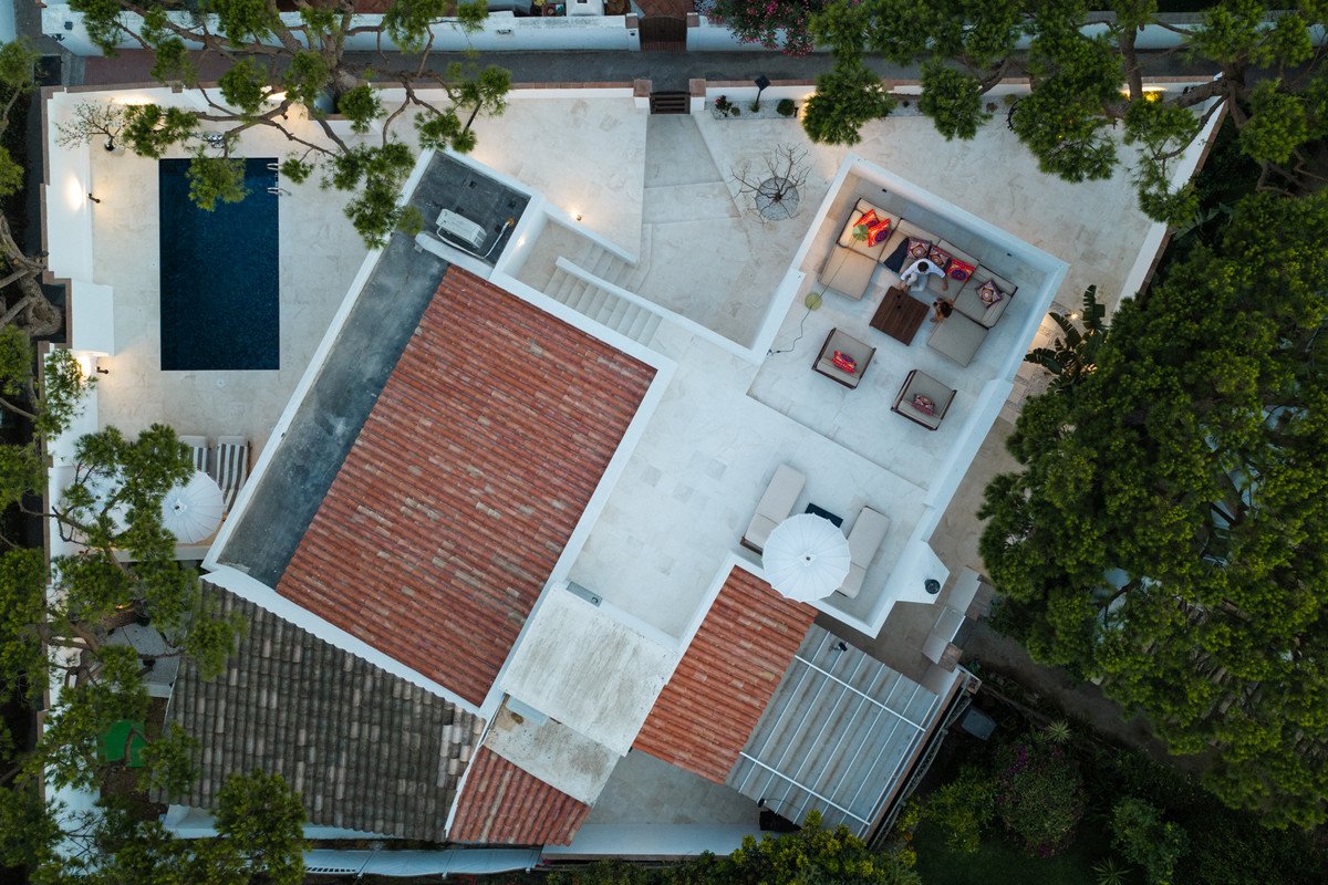 Aerial view of a modern villa with a pool, terraces, and red-tiled roofs surrounded by greenery.