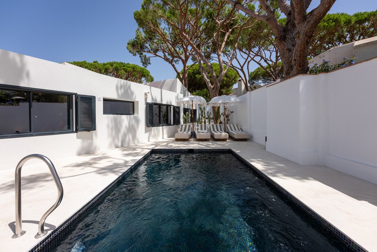 Modern villa with private pool, lounge chairs, and shaded seating under trees.
