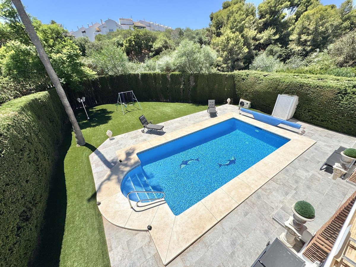 Lush green lawn with a swing set and a pristine swimming pool with steps, surrounded by tall hedges and trees.
