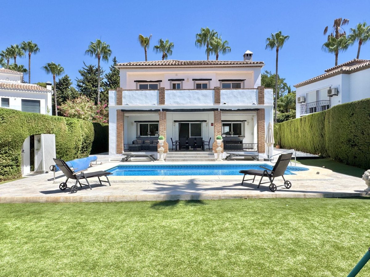 A villa with a private swimming pool, patio, lounge chairs, and palm trees on a sunny day.