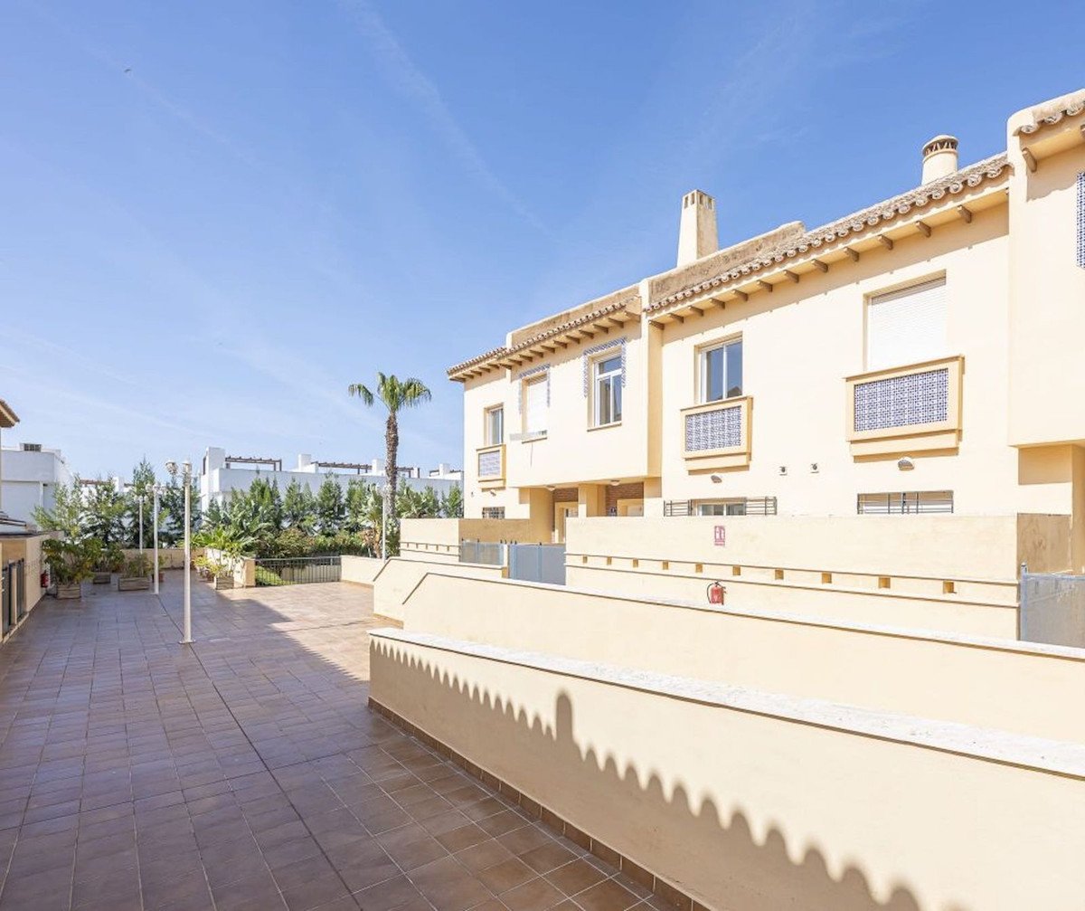 Terraced houses with palm trees and a blue sky, featuring tiled patio areas and decorative window elements.