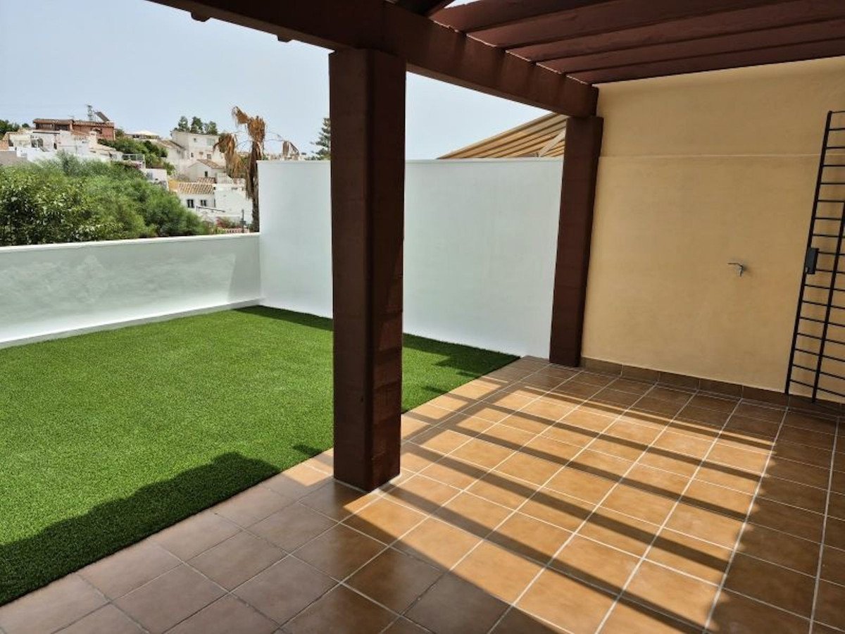 A terrace with artificial grass and tiled area, featuring a pergola and views of a hillside town.