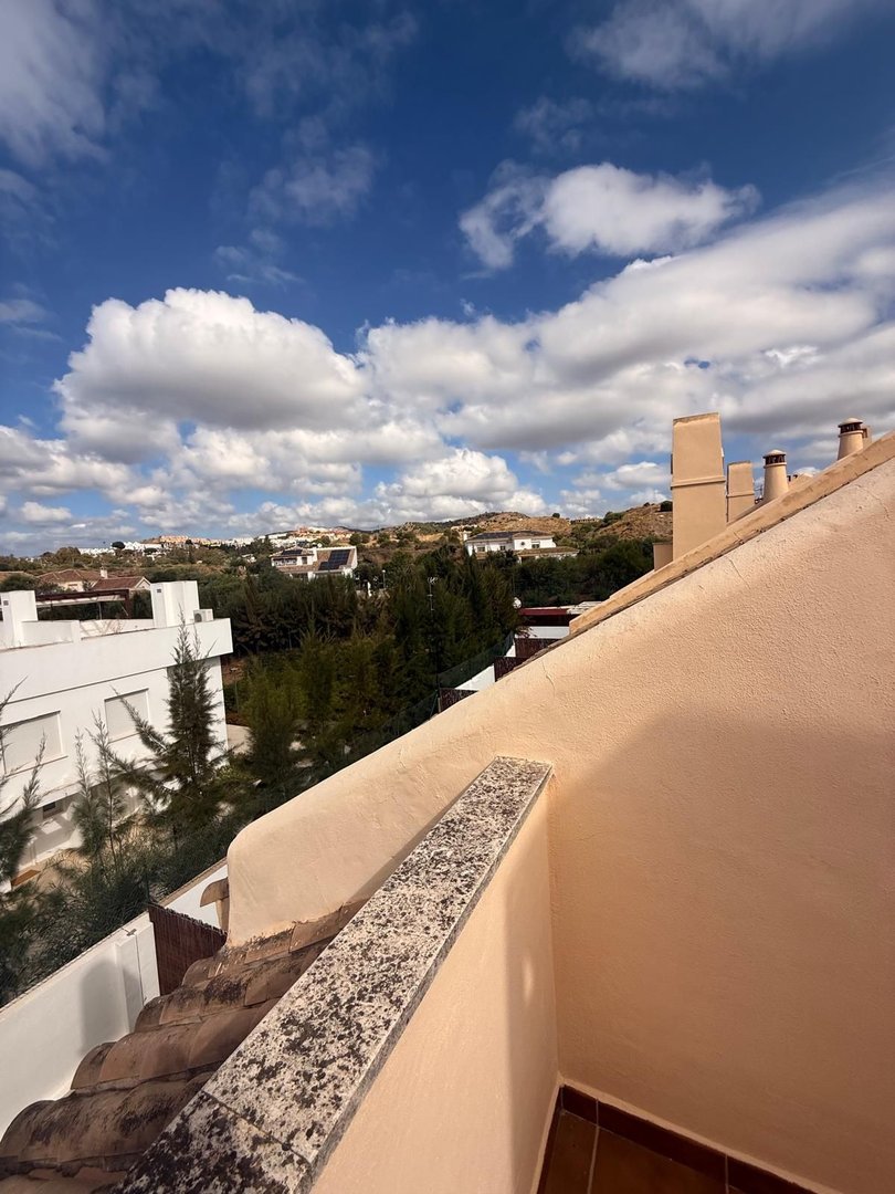 Terrace view overlooking houses and green trees under a bright blue sky with fluffy white clouds.