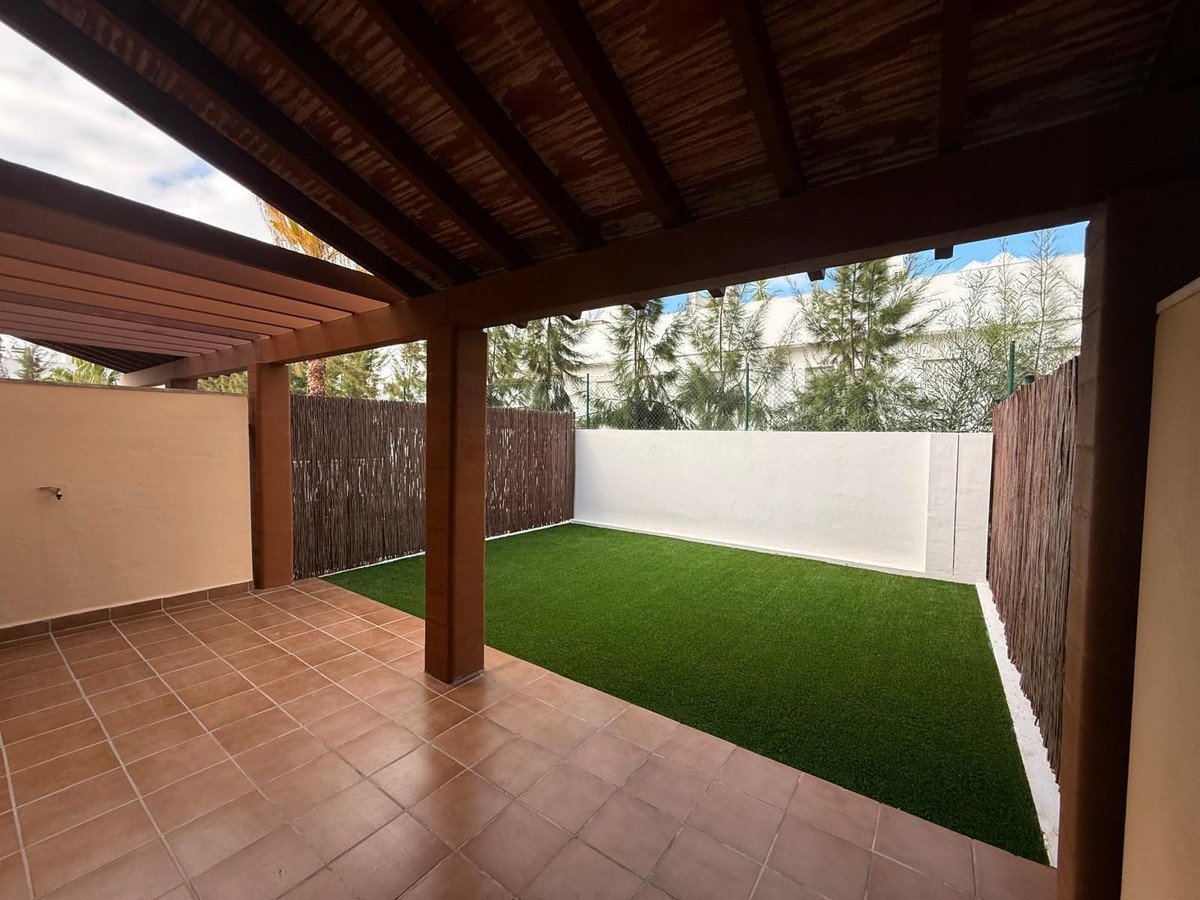Terrace with tiled floor and artificial lawn leading to a backyard with bamboo fencing and lush green trees visible.
