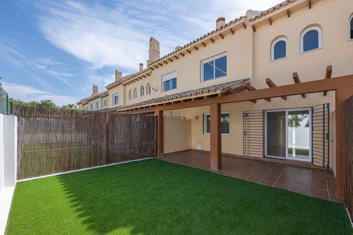 A modern townhouse with a covered patio, artificial grass backyard, and bamboo fence under a blue sky.
