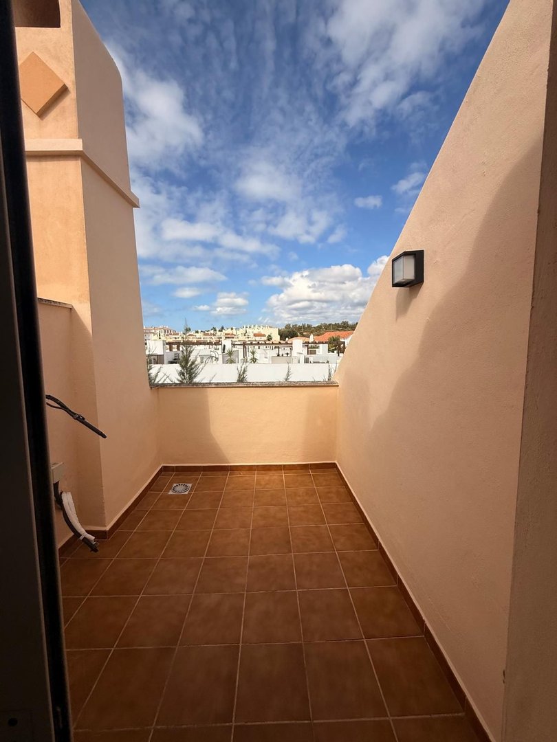 A small, tiled terrace with a view of a town skyline under a cloudy blue sky.