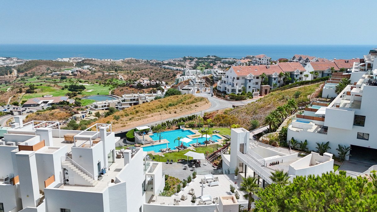 Resort complex with swimming pools, manicured gardens, golf course, and distant sea view under a clear blue sky.