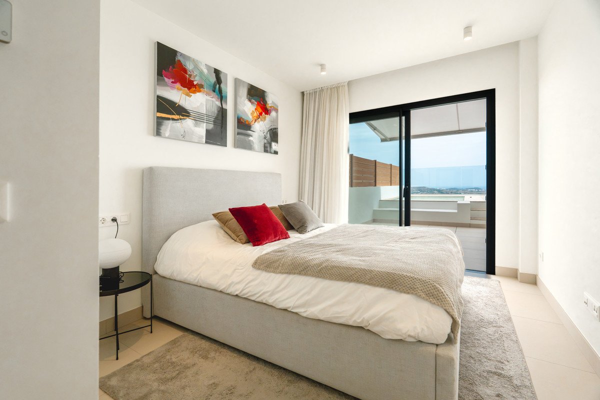 Modern bedroom with a large bed, abstract art, and sliding glass doors leading to a balcony with a sea view.