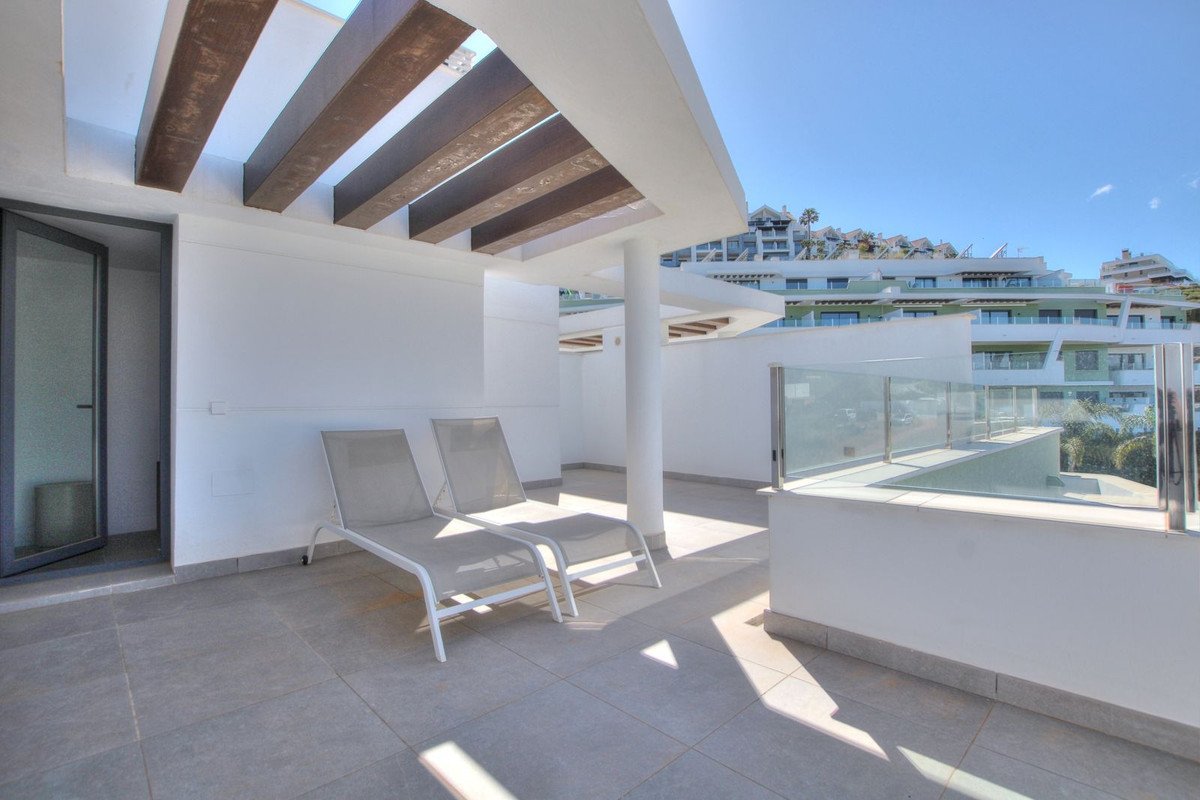 Modern terrace with two lounge chairs, glass railing, and a view of a resort complex.