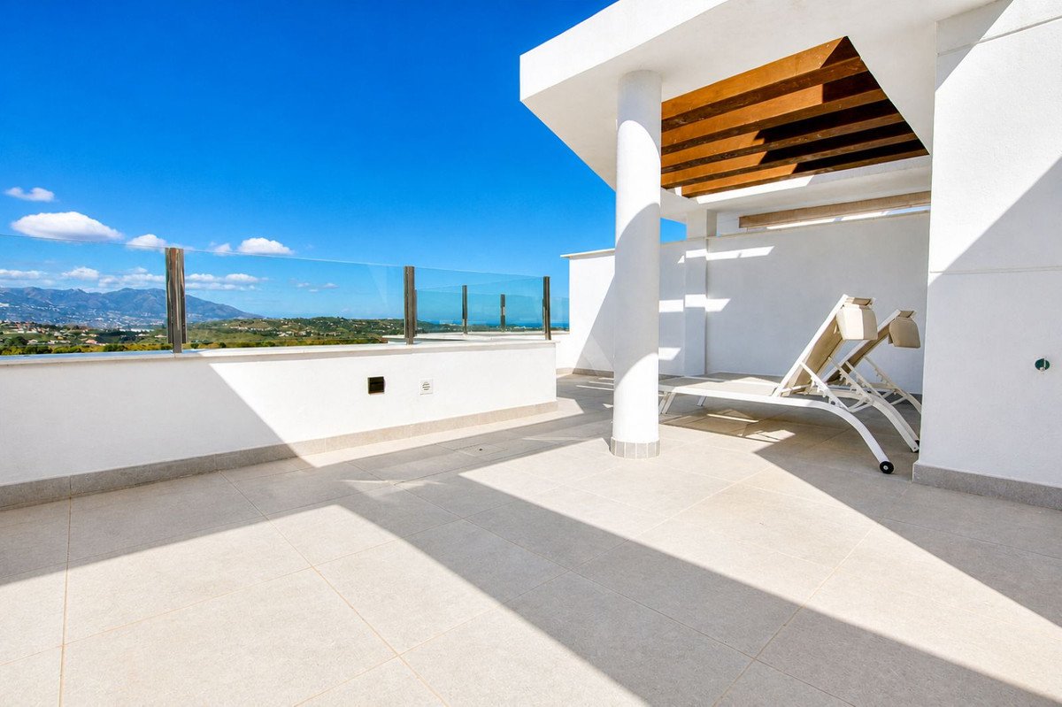 Spacious terrace with glass balustrade offering a sea view, featuring sun loungers and modern architecture under a clear blue sky.