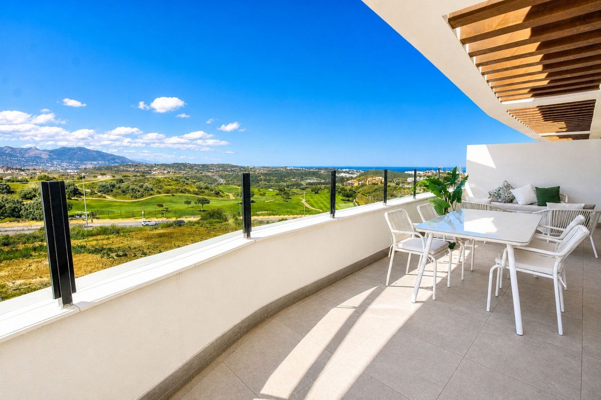 Spacious terrace with dining set and lounge area overlooking a golf course and the sea under a blue sky.