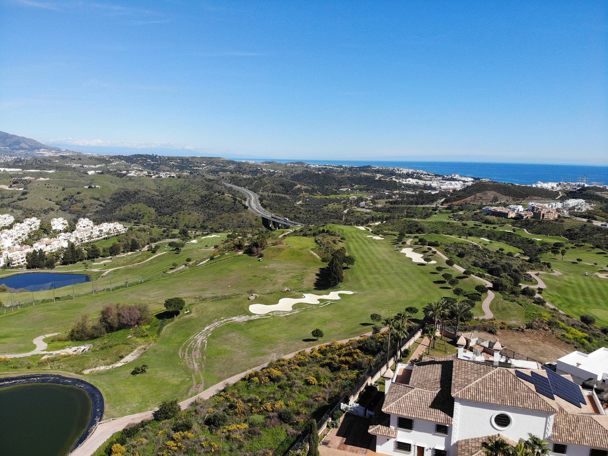 Aerial view of a luxury villa with solar panels, overlooking a golf course and the Mediterranean Sea.