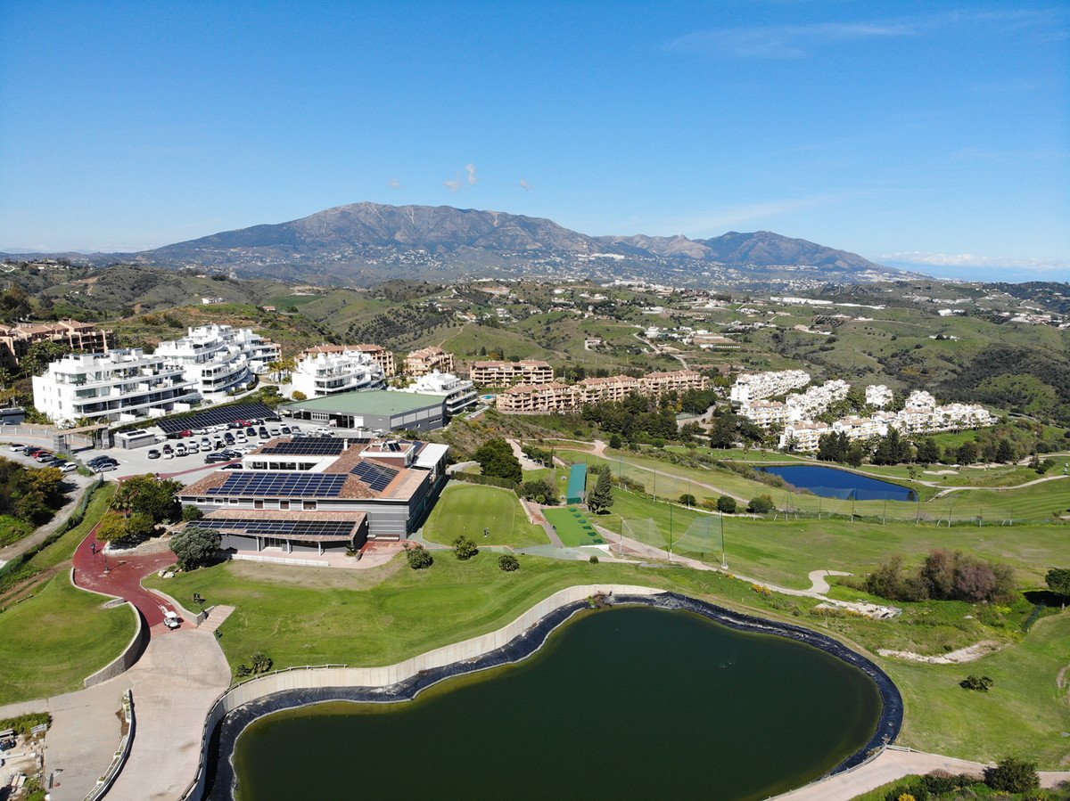 Aerial view of a resort with golf course, lakes, and mountain backdrop under clear blue sky.