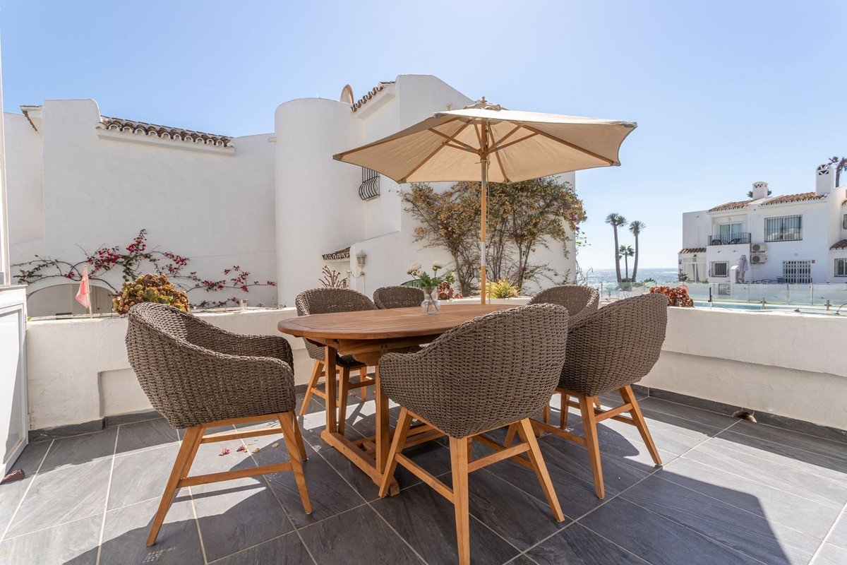 Outdoor dining set with chairs and umbrella on a balcony with a view of the sea and buildings.